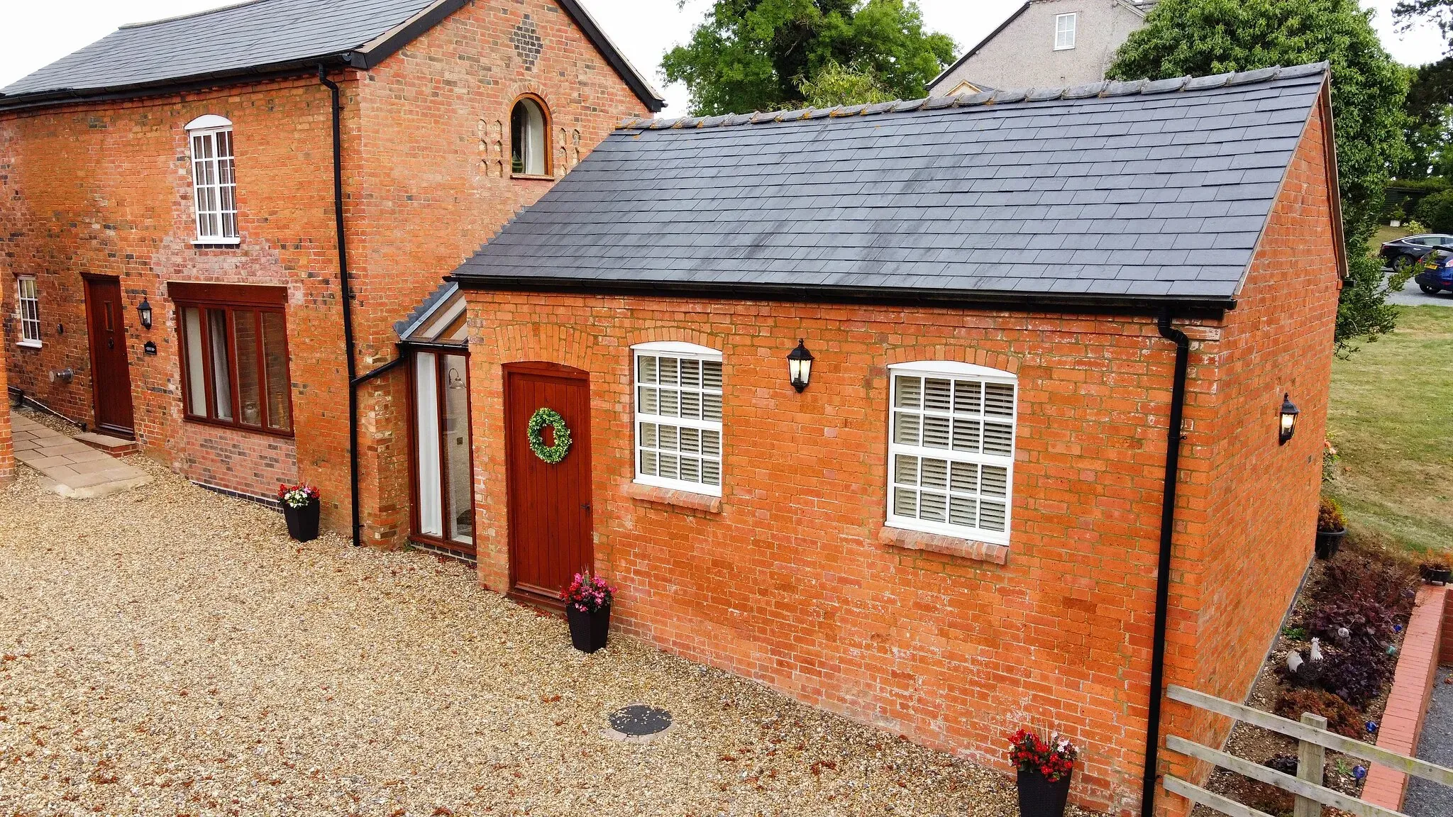 Chestnut Barn's single-storey red brick frontage across the gravel courtyard, with Oak Barn behind